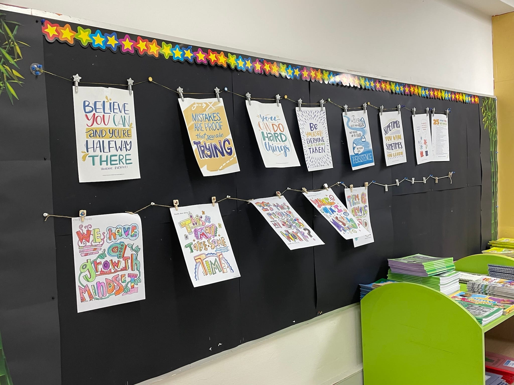 Colorful motivational posters clipped to strings on a black bulletin board with star decorations in a classroom.